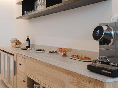 Buffetruimte met koffiezetapparaat en diverse snacks op een marmeren aanrechtblad in een lichte houten inrichting.