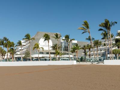 Hotelgebouw met palmbomen op het strand onder een heldere blauwe lucht.