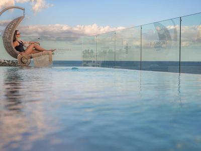 Vrouw ontspant in hangstoel naast infinity pool met uitzicht op zee bij zonsondergang.