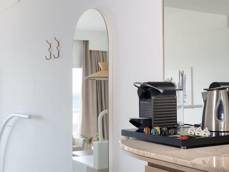 Moderner Küchenbereich mit Kaffeemaschine, Wasserkocher auf Holzarbeitsplatte, Spiegel und Haken an weißer Wand.