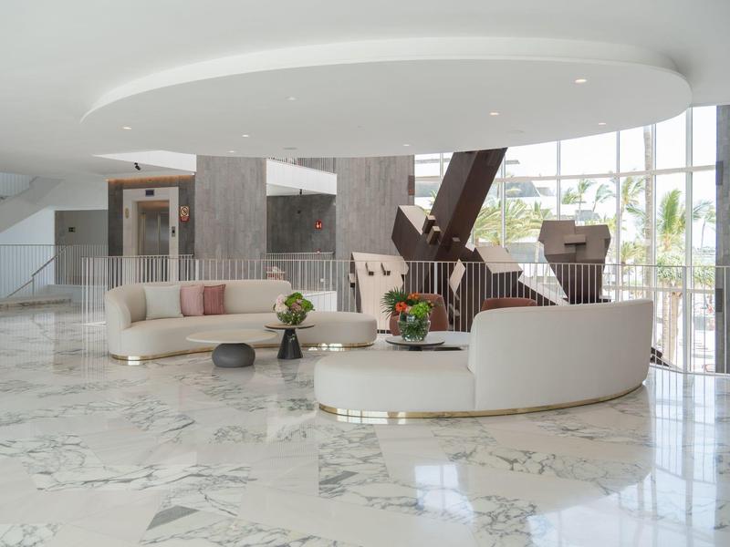 Moderner, heller Empfangsbereich mit weißem Marmorboden, runden Sofas und großer Glasfront.