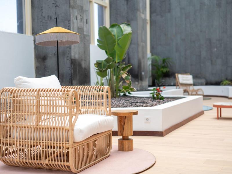 Moderner Außenbereich mit hellem Rattansessel, weißem Kissen und kleinem Holztisch.