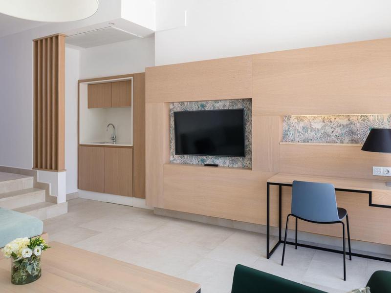 Moderner Wohnraum mit hellen Wänden, TV, Schreibtisch, Stuhl und Treppe, helle Fliesen auf dem Boden.