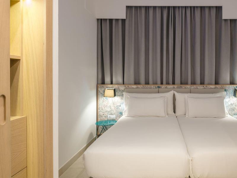 Modernes Hotelzimmer mit zwei Einzelbetten, grauem Vorhang und Holzschrank an der Wand.