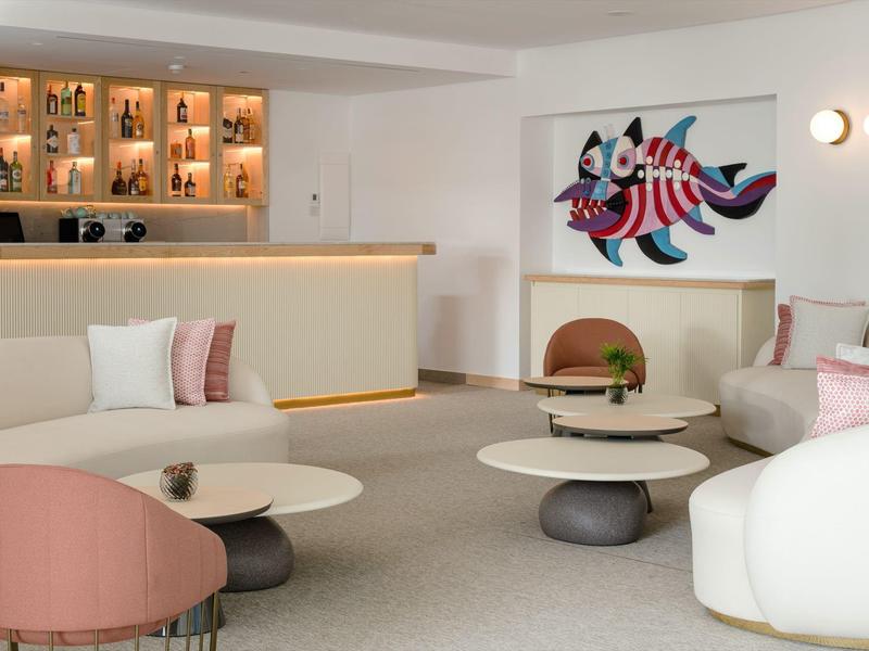 Moderner Raum mit weißen Sofas, rosa Stuhl, runden Tischen und farbiger Katzenwandkunst.