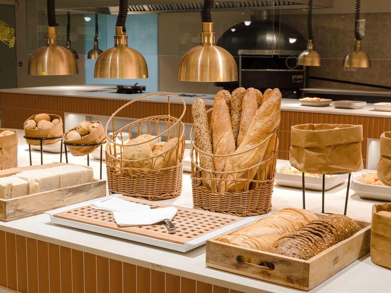 Bäckerei-Theke mit verschiedenen Broten, Körben und warmem Licht unter Kupferlampen.
