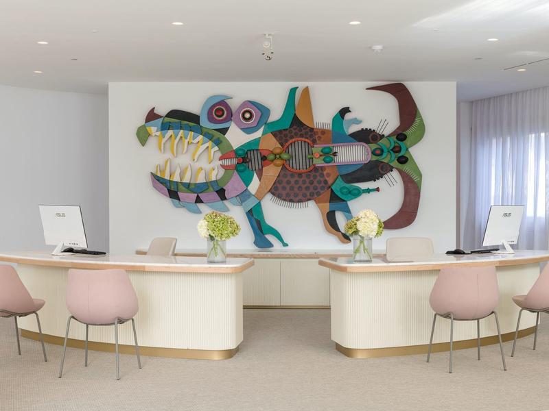 Moderner Empfang mit zwei weißen Tischen, sechs rosa Stühlen und farbenfroher abstrakter Wandkunst.