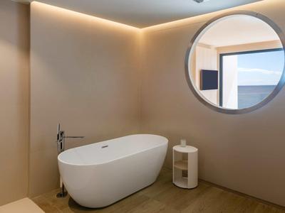 Moderne Badezimmerecke mit freistehender weißer Badewanne, kleinem runden Regal und rundem Spiegel.