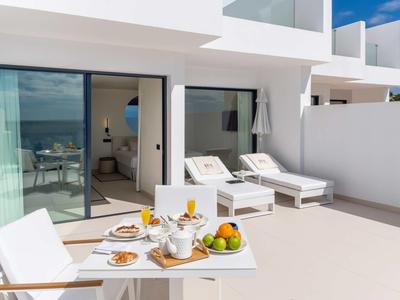 Dachterrasse mit weißer Lounge, zwei Liegestühlen, Obstkorb und Frühstück bei sonnigem Himmel.