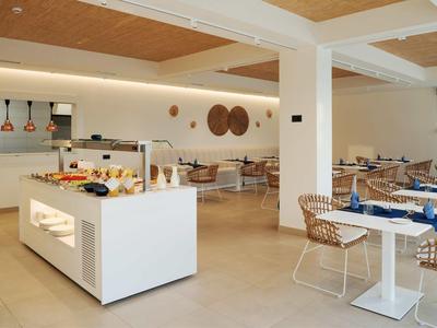 Moderner Speiseraum mit weißen Tischen, Stühlen aus Korbgeflecht und Buffetinsel in hellem Design.