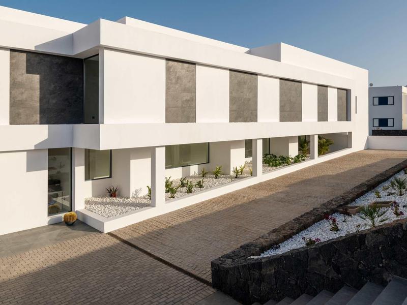 Moderner Gebäudekomplex mit weißen Fassaden, großen Fenstern und heller Terrasse bei klarem Himmel.