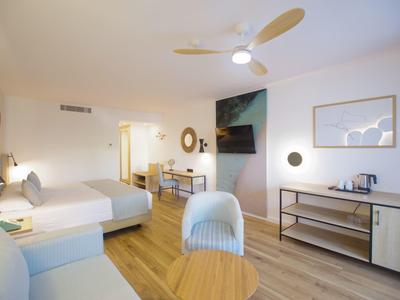 Moderner Hotelraum mit hellem Holzboden, großem Bett, Fernseher, Schreibtisch und Sitzbereich.