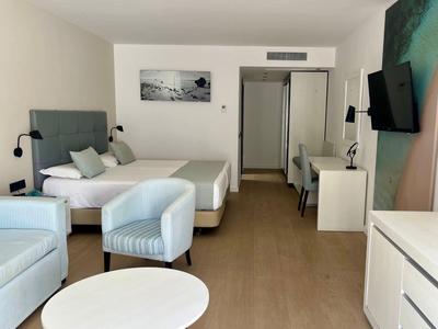 Helles Hotelzimmer mit zwei Betten, Sesseln, Schreibtisch, TV und modernem Holzboden.