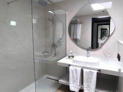 Moderne Badezimmer mit weißer Marmorwand, runder Spiegel, Glasdusche und zwei weißen Handtüchern.