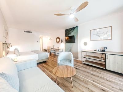 Helles Wohnzimmer mit weißem Sofa, Sesseln, Holzboden und moderner Deckenlampe.