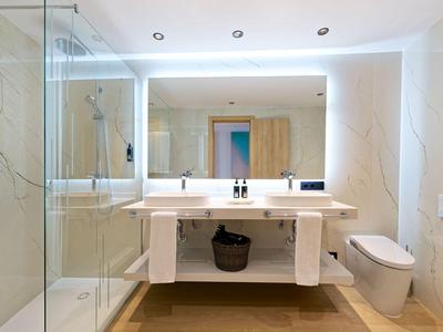 Nowoczesna łazienka z dużym podświetlanym lustrem i prysznicem.