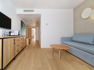 Nowoczesny pokój hotelowy z drewnianą podłogą, niebieską sofą i telewizorem na ścianie.