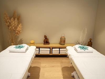 Deux tables de massage avec serviettes blanches dans une pièce calme et éclairée chaleureusement.