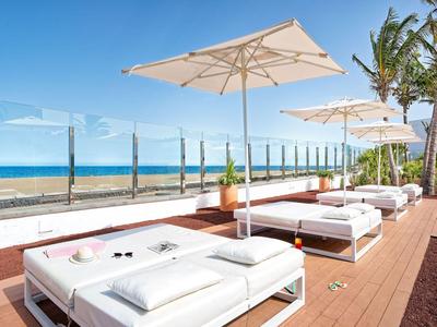 Transats blancs avec parasols sur une terrasse donnant sur la mer par une journée ensoleillée.