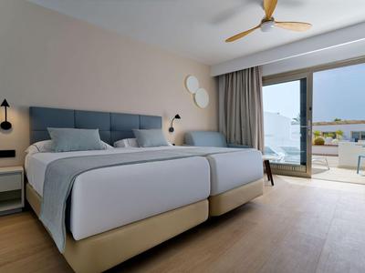 Chambre d'hôtel moderne avec deux lits simples, coin salon et accès à un balcon avec vue.