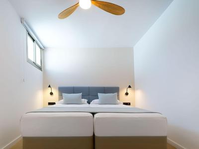 Lit double simple et moderne dans une chambre d'hôtel lumineuse et minimaliste avec ventilateur de plafond.