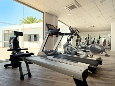 Salle de sport lumineuse avec tapis roulants et appareils d'exercice près de grandes fenêtres.