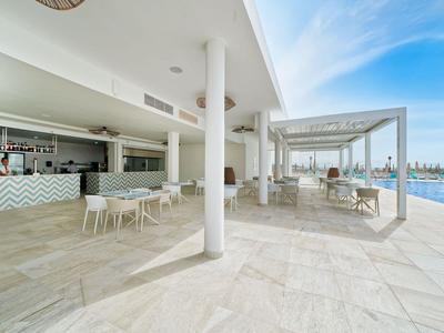 Espace extérieur moderne avec bar, sièges et piscine sous un ciel bleu.