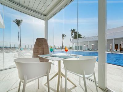Espace extérieur moderne avec piscine, chaises blanches et table en verre sous toit en verre.