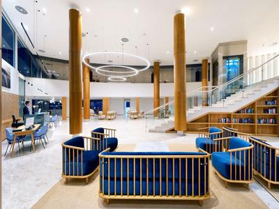 Hall d'hôtel lumineux et moderne avec fauteuils bleus, éléments en bois et grand tapis.