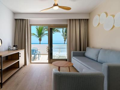 Chambre d'hôtel moderne avec balcon et vue sur la mer, équipée d'un canapé et de meubles en bois.