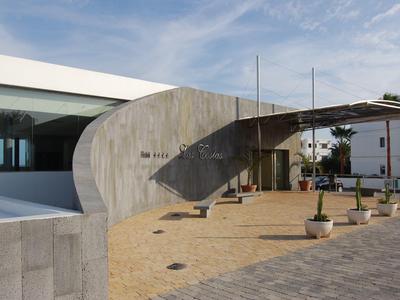 Moderner Gebäudeeingang mit geschwungener Betonwand, Glasfenstern und gepflastertem Platz.