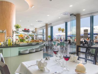 Helles Restaurant mit großen Fenstern, gedeckten Tischen und Buffetbereich am Fenster.