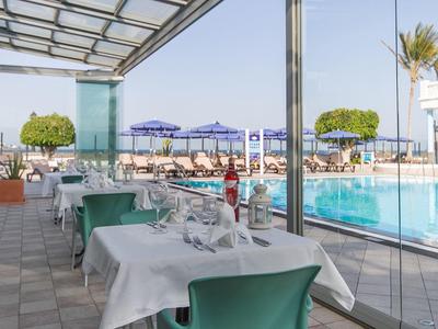 Außenbereich eines Restaurants mit gedeckten Tischen, grünen Stühlen und Blick auf einen Pool und Strand.