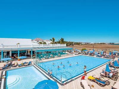 Schwimmbadbereich mit Rechteck- und Kinderbecken, vielen Sonnenschirmen, Liegestühlen und blauem Himmel.