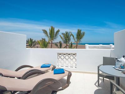 Terrasse mit zwei beige Liegestühlen, blauen Handtüchern und kleinem Tisch bei blauem Himmel.