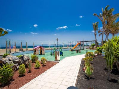 Basen hotelowy z zjeżdżalniami wodnymi, otoczony palmami, widok na morze pod słonecznym niebem.