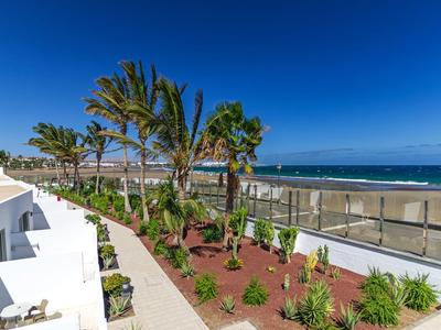 Vue sur un jardin d'hôtel avec des palmiers et la mer en arrière-plan sous un ciel dégagé.