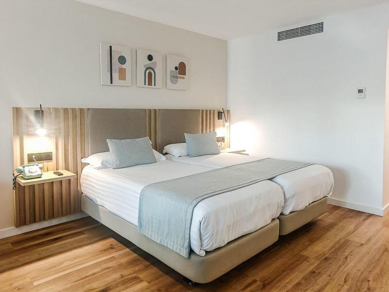 Hell eingerichtetes Doppelzimmer mit zwei Einzelbetten, Holzboden und minimalistischer Dekoration.