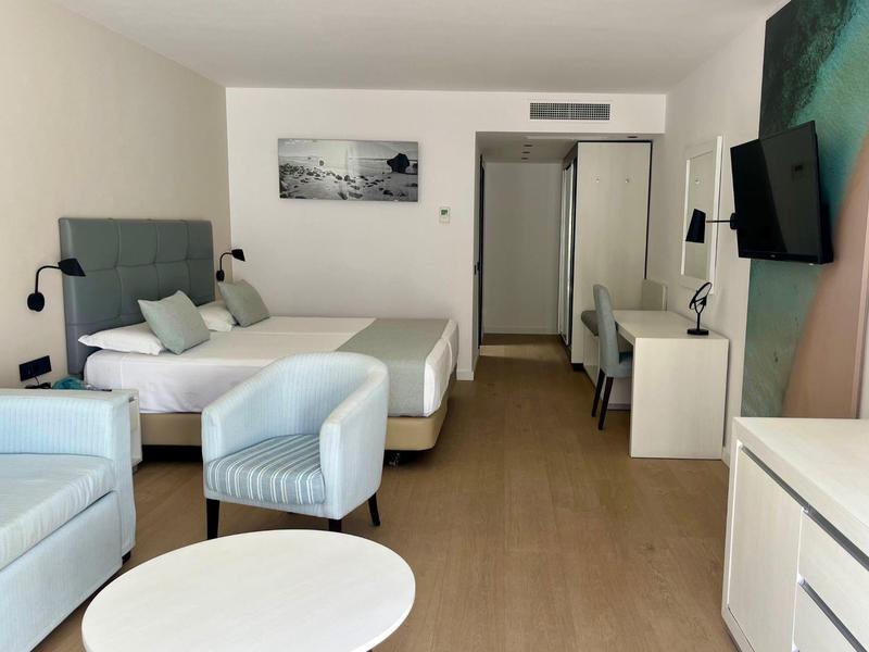 Helles Hotelzimmer mit zwei Betten, Sesseln, Schreibtisch, TV und modernem Holzboden.