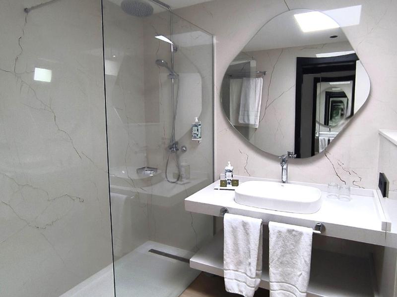 Moderne Badezimmer mit weißer Marmorwand, runder Spiegel, Glasdusche und zwei weißen Handtüchern.