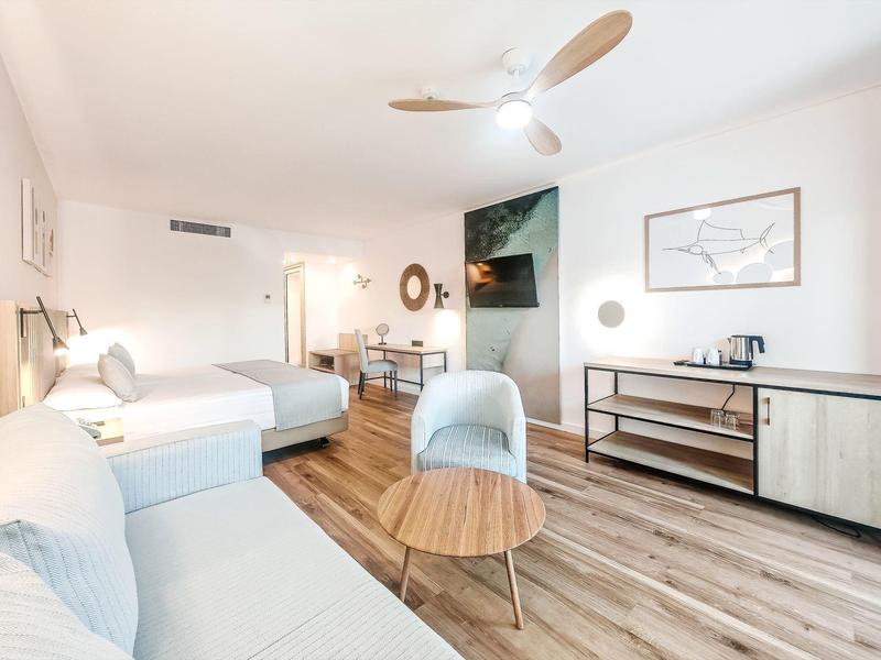 Helles Wohnzimmer mit weißem Sofa, Sesseln, Holzboden und moderner Deckenlampe.