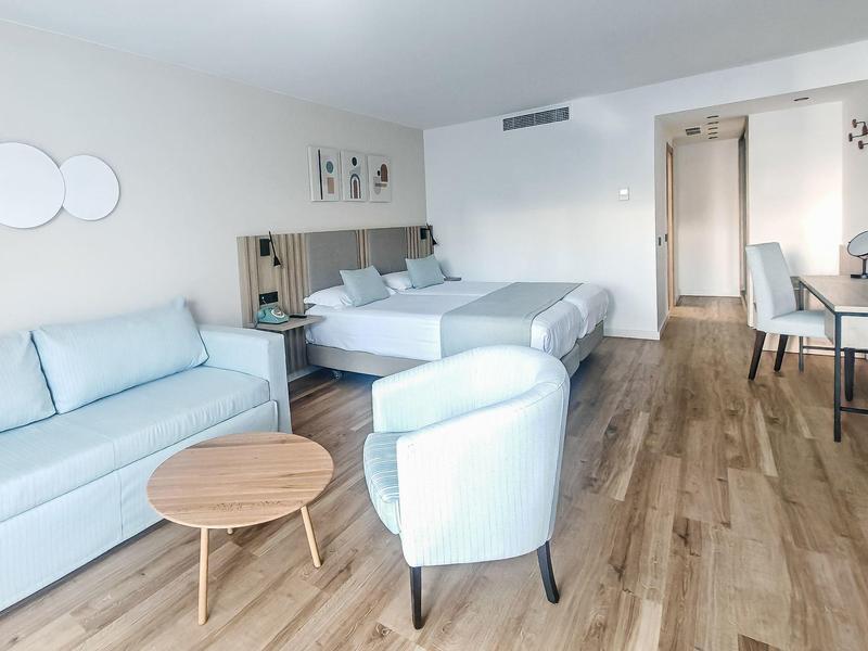 Modernes Hotelzimmer mit zwei Betten, hellblauem Sofa, Sesseln und Holzboden.