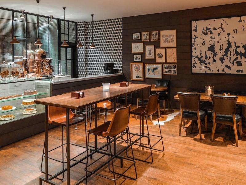 Modernes Café mit Holzfußboden, hohen Tischen, Stühlen und Vitrine voller Backwaren.