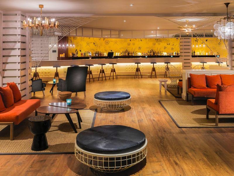 Moderner Lounge-Bereich mit orangen Sesseln, schwarzen Hockern und hellen Holzböden.