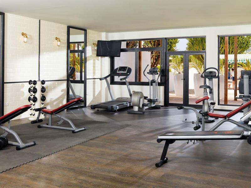 Heller Fitnessraum mit Geräten, Hantelbank, Laufband und großen Fenstern zum Garten hin.