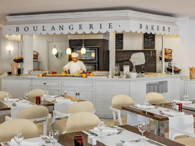 Hell eingerichtetes französisches Bäckerei-Café mit Tischen, Stühlen und einem Bäcker hinter der Theke.