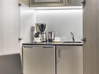 Angolo cottura compatto in camera d'hotel con microonde, macchina per caffè e mini frigorifero.