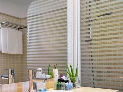 Bagno dell'hotel moderno con lavabo, rubinetto, articoli da toilette e piante sul piano.