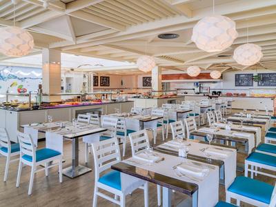 Ristorante spazioso con sedie bianche, cuscini blu e tavoli di legno apparecchiati.