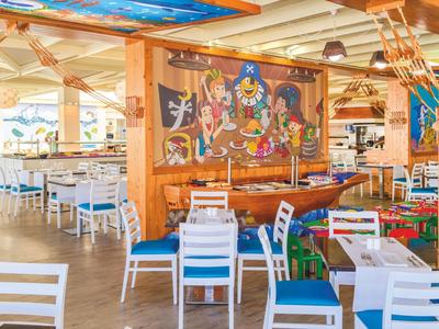 Ristorante luminoso a tema nautico con sedie bianche, cuscini blu e murale cartoon.